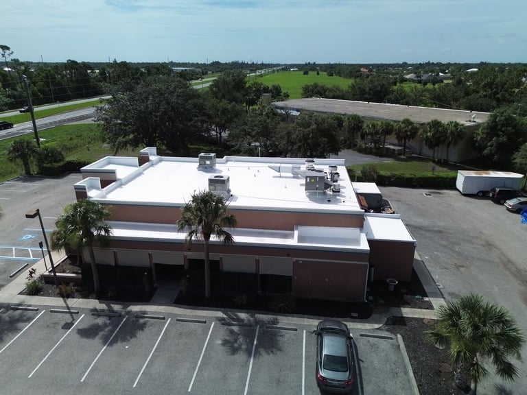Drone view of a finished white commercial flat roof with rooftop HVAC and exhaust fans on a stucco restaurant