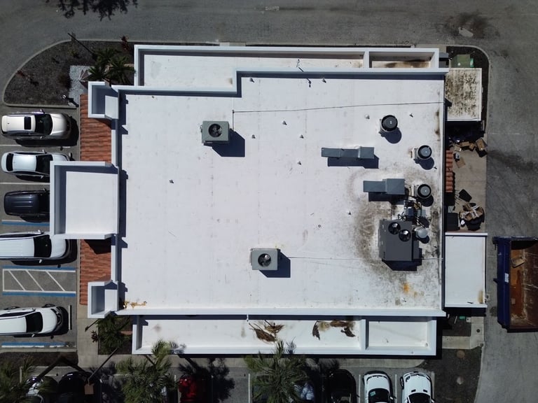 Top-down view of a stained, weathered commercial flat roof on a restaurant before roof replacement
