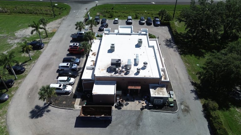Overhead view of a restaurant's stained flat roof and roll-off dumpster at the start of a roof replacement