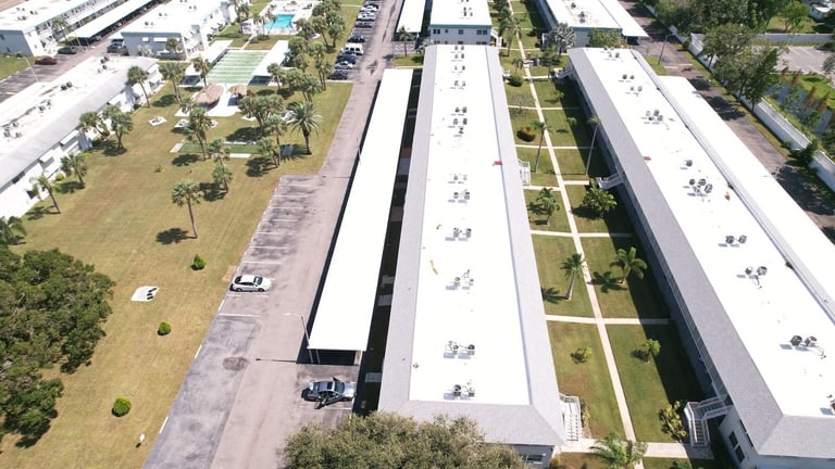 Drone view of new white TPO flat roofs on long two-story condo buildings with carports and courtyards