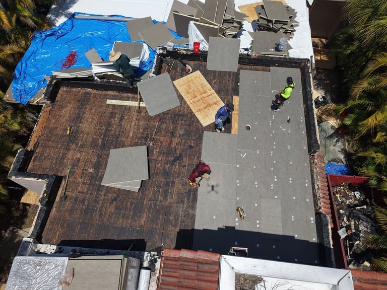 Roofing crew fastening gray insulation cover boards over the wood deck during a flat roof replacement