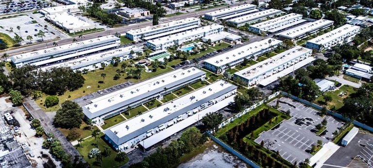 Aerial of multifamily buildings, carports and parking areas with white TPO flat roofs
