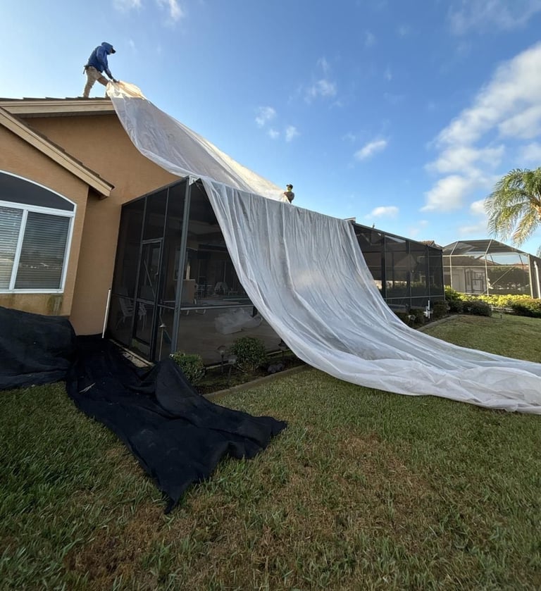 Roofer rolling protective plastic sheeting off the roof to shield a screened lanai and lawn before tile roof tear-off