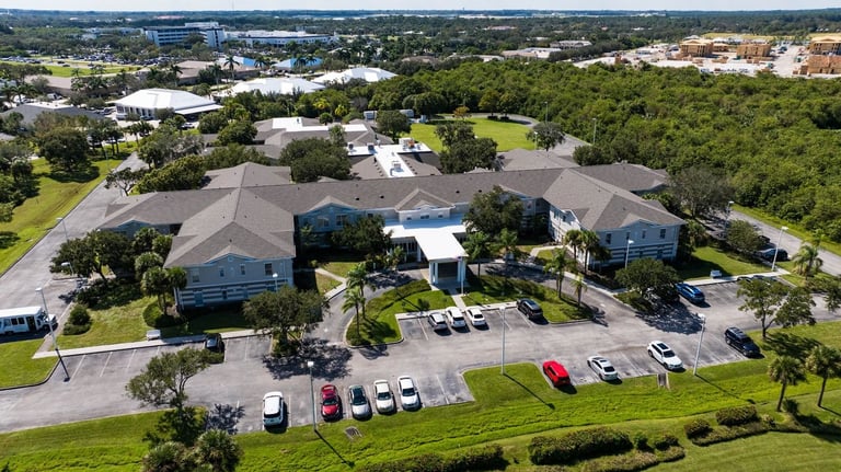 Wide aerial of an assisted living campus with new gray shingle roofs above a large parking lot