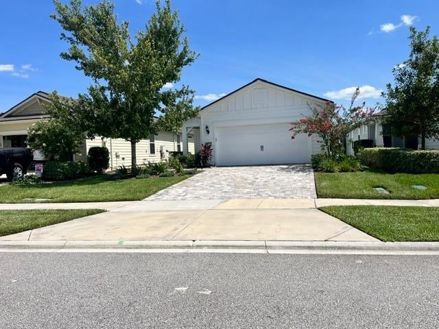 Modern single-story beige house with white garage door, concrete driveway, and landscaped lawn on sunny day