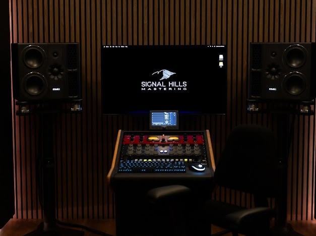 Professional music production studio setup with Signal Hills monitor display, large speakers, mixing console, and red acoustic panels