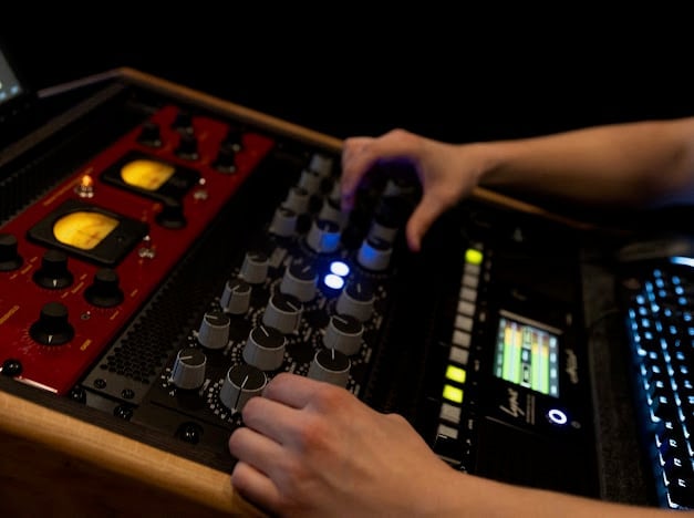DJ hands operating electronic music production equipment with illuminated knobs and controls on a mixer console