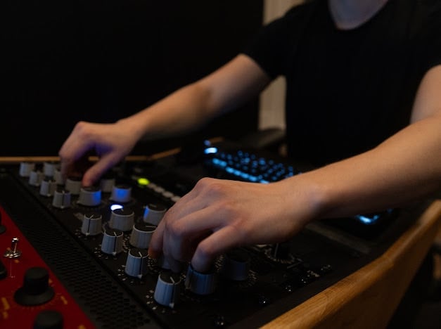DJ operating a mixing console with illuminated buttons and knobs during a performance in dim lighting