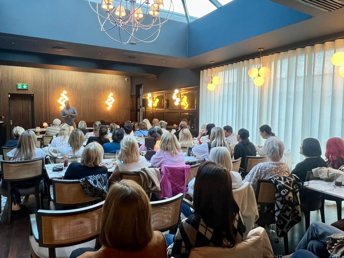 Large group of women seated at round tables in an elegant dining room with blue ceiling and modern chandeliers