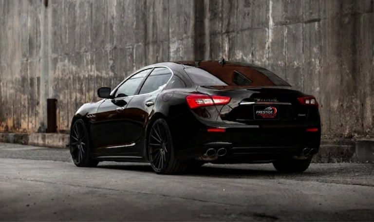 Sleek black sports sedan parked against a weathered concrete wall, rear quarter view highlighting its sporty design and taillights