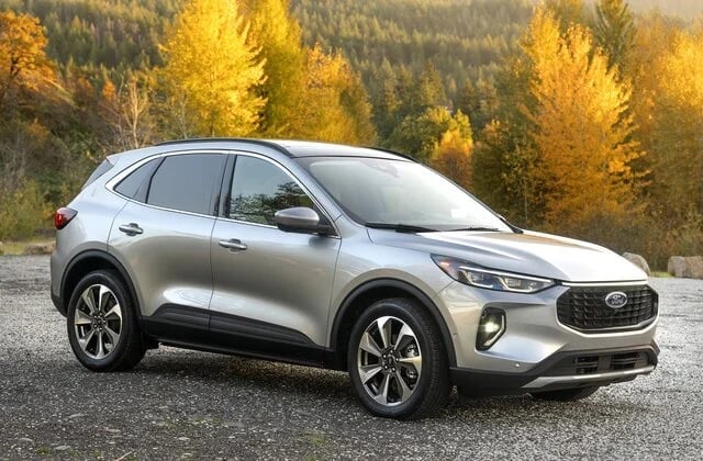 Silver compact SUV parked on gravel with golden autumn trees and forest in the background