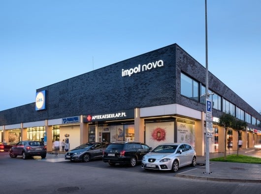 Modern Imol Nova shopping mall exterior at dusk with illuminated storefronts and parked vehicles in front