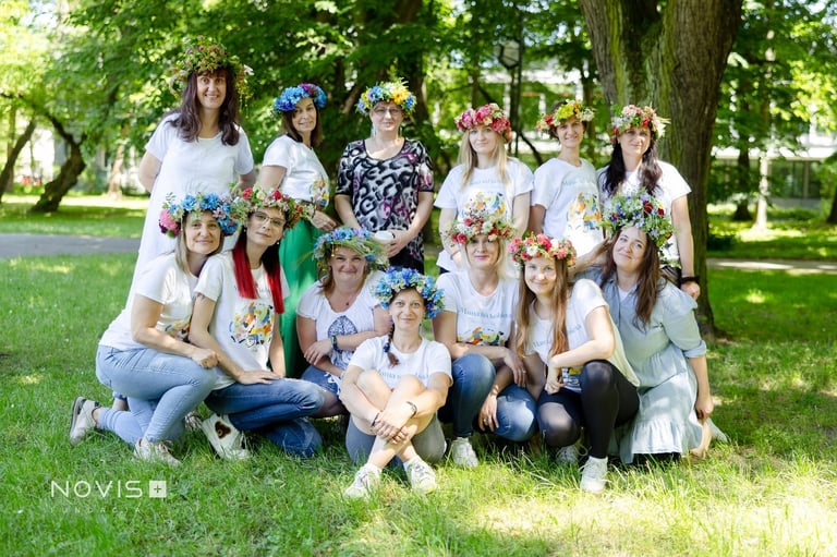 Large group of women wearing white shirts and flower crowns posing together on grass in a park