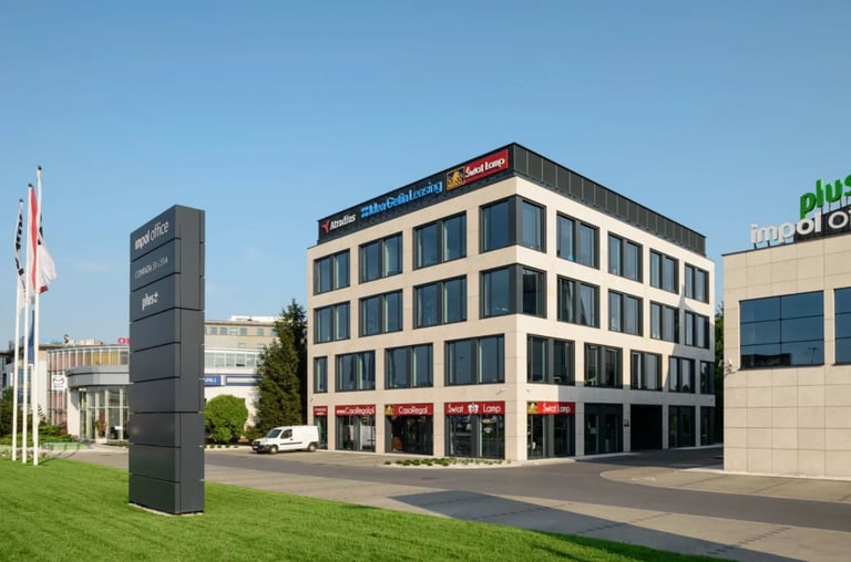 Modern multi-story commercial building with cream and dark blue facade, red storefronts on ground level, and a dark monolith sign in foreground