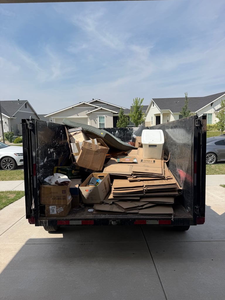 Open dumpster truck filled with cardboard boxes and debris in a residential neighborhood.