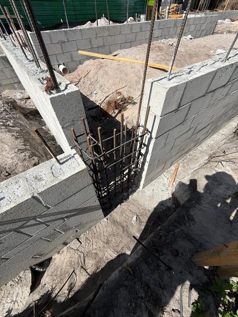 Construction site with concrete foundation walls, reinforcement rebar, and building materials under development