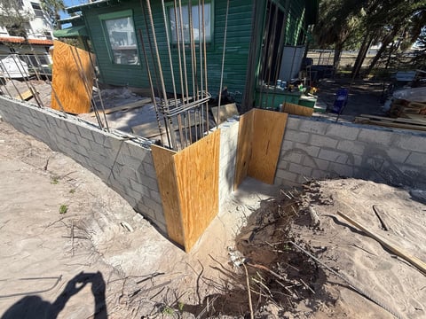 Green trailer with wooden door and gate under construction on concrete foundation surrounded by dirt