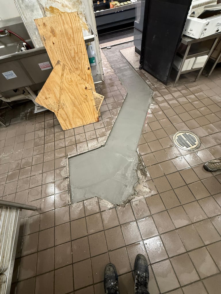 Flooded commercial kitchen floor with gray water pooling around tiles, wooden plywood barrier, and restaurant equipment in background
