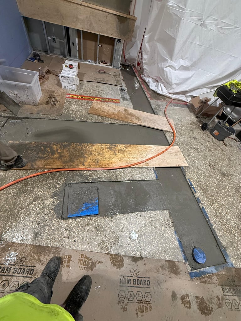 Construction site flooring installation with tile samples, extension cord, and protective plastic sheeting on concrete subfloor