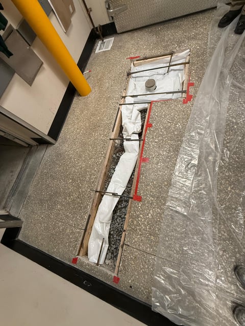 Overhead view of a construction layout with red guide lines, metal framing, and white insulation material on concrete floor