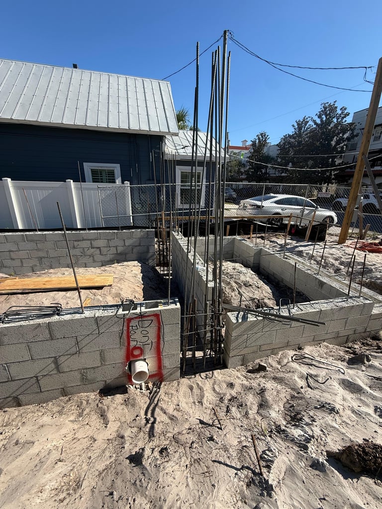 Construction site with concrete foundation walls, steel reinforcement rebar cage, and red hydraulic equipment in a residential area
