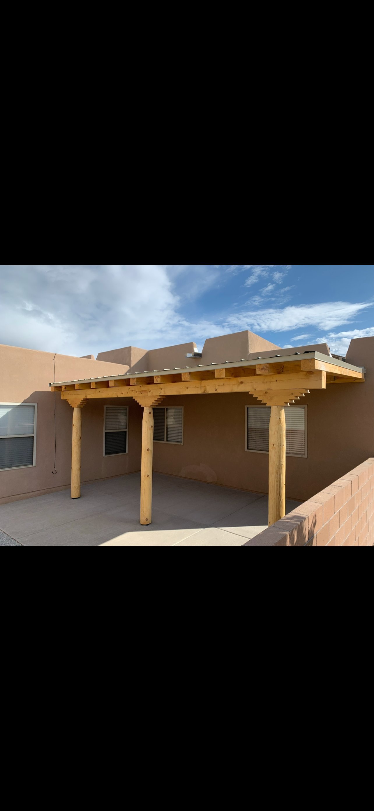 Custom wooden pergola attached to a tan stucco house under a blue sky