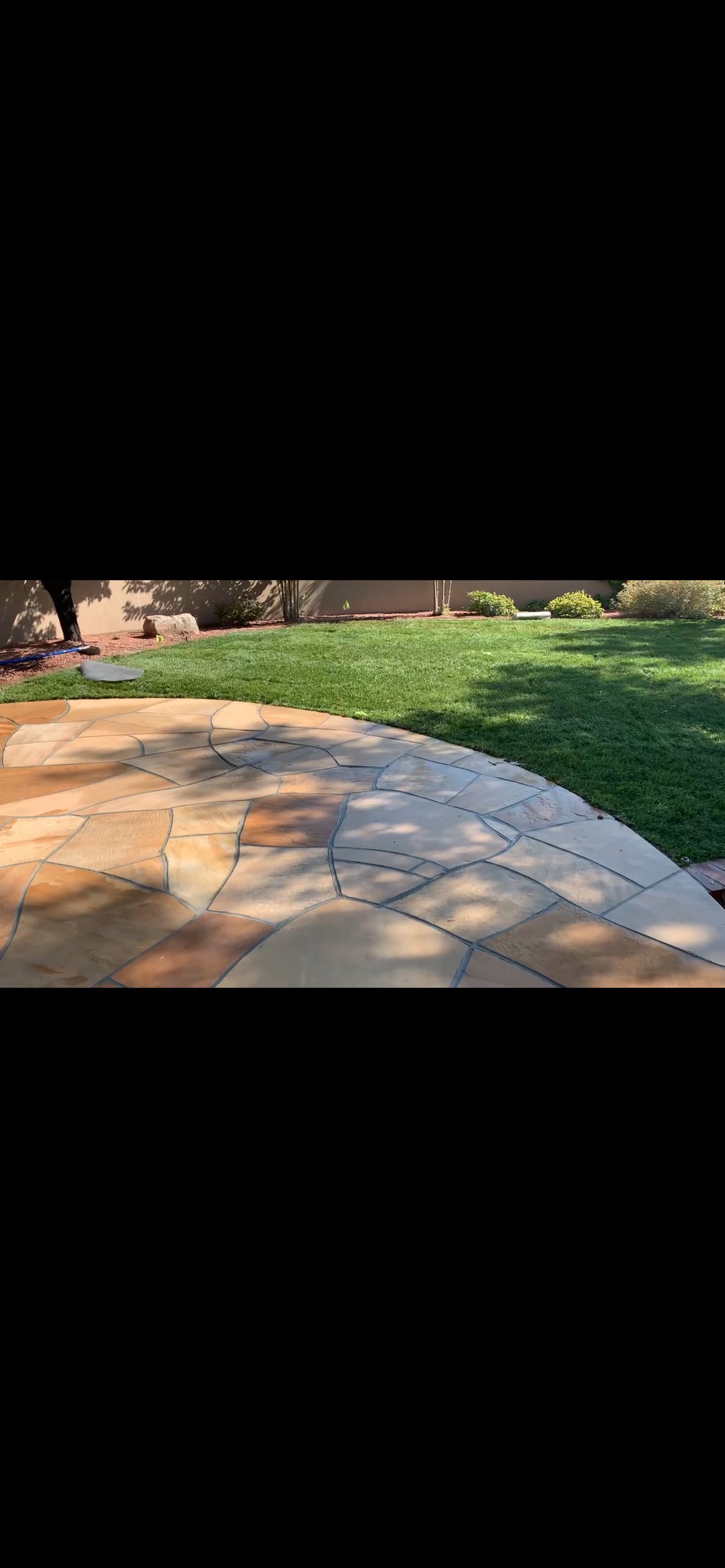 Curved flagstone patio with geometric patterns in a sunny backyard with green lawn