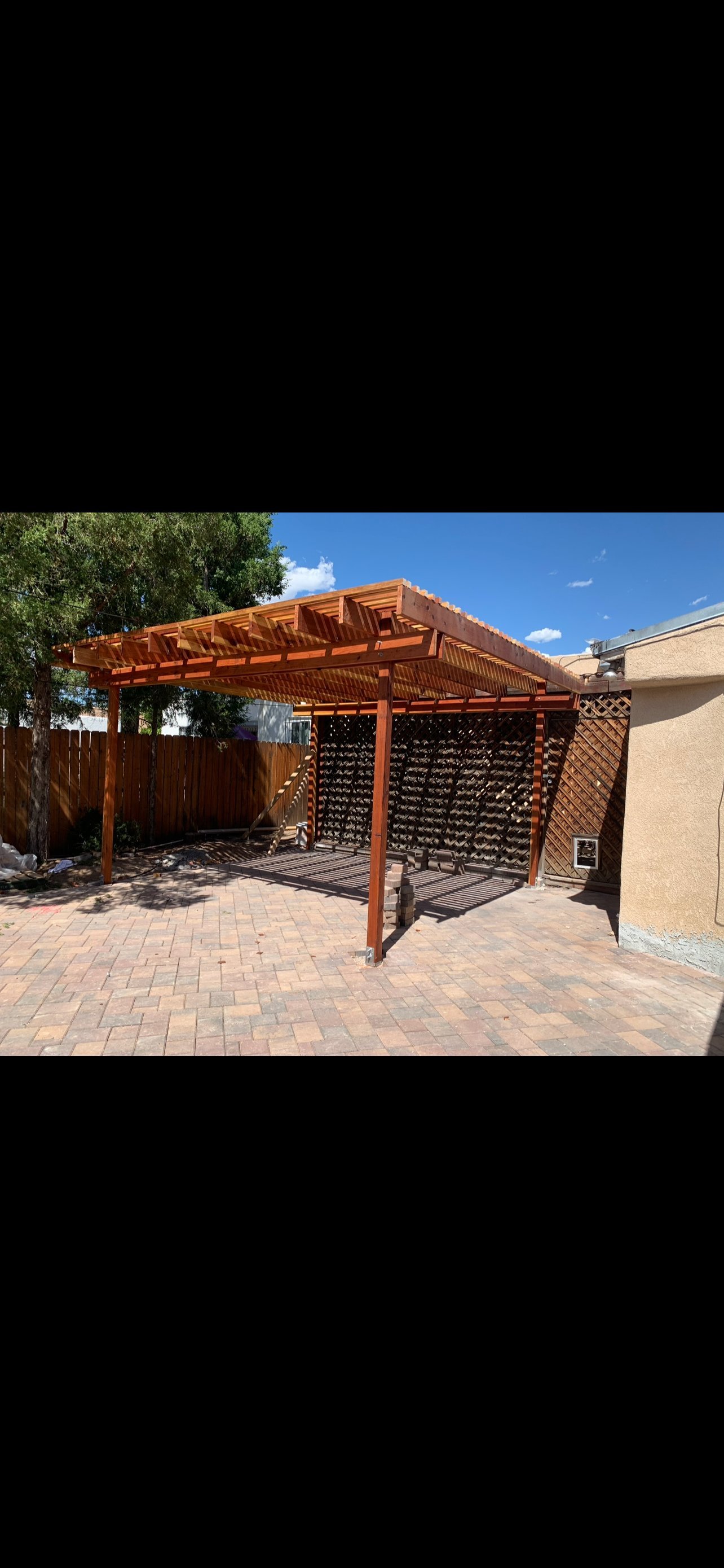 Wooden pergola with lattice walls on a brick patio, adjacent to a tan stucco building