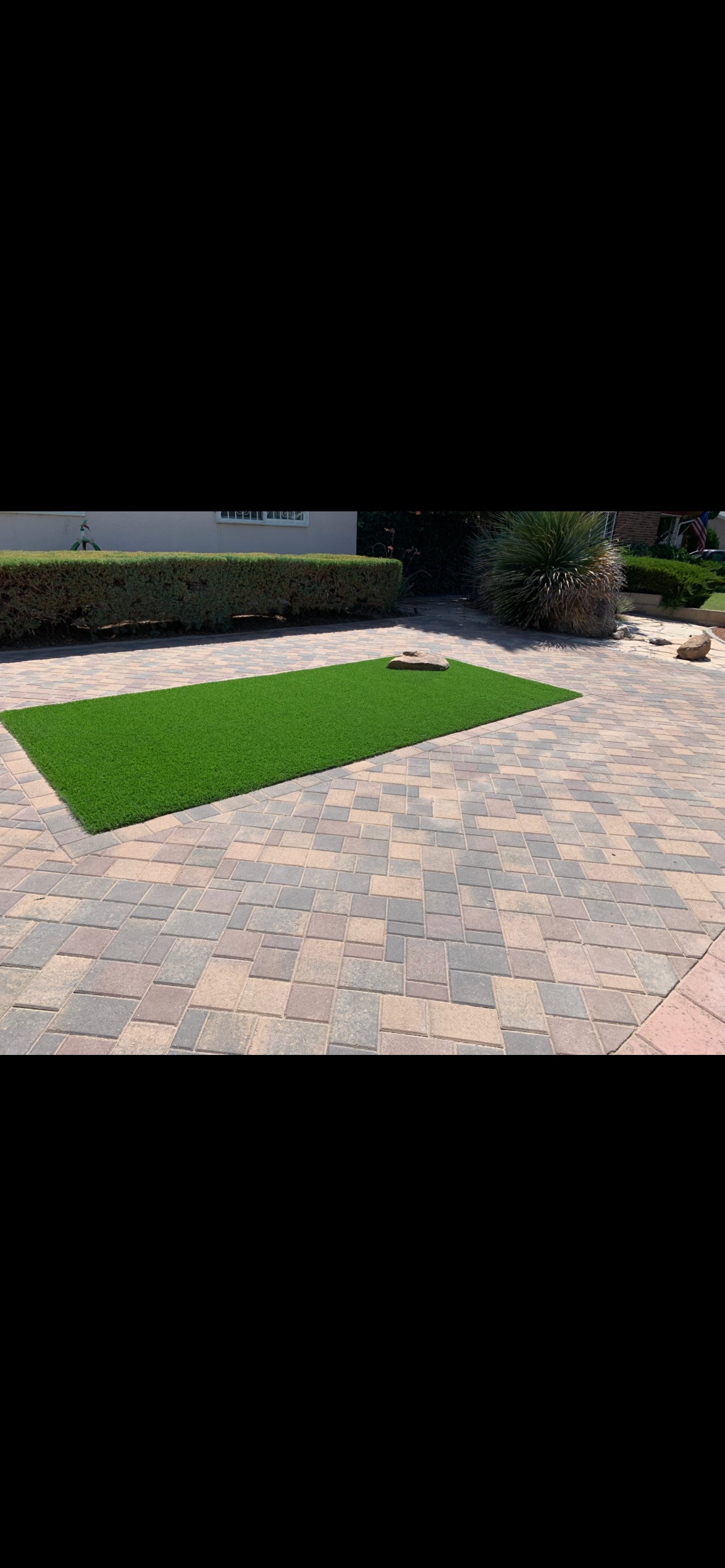 Residential patio with artificial turf rectangle on a paver surface, bordered by hedges