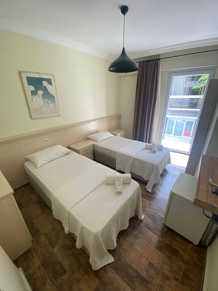 Hotel room with two twin beds, yellow walls, pendant light, and glass doors opening to a balcony with ocean view