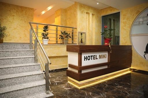 Hotel Miki reception desk in modern lobby with yellow walls, marble flooring, staircase, and contemporary lighting