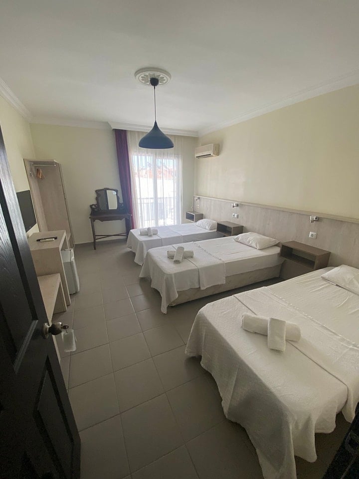 Triple bed hotel room with white bedding, pendant light, and large windows with curtains
