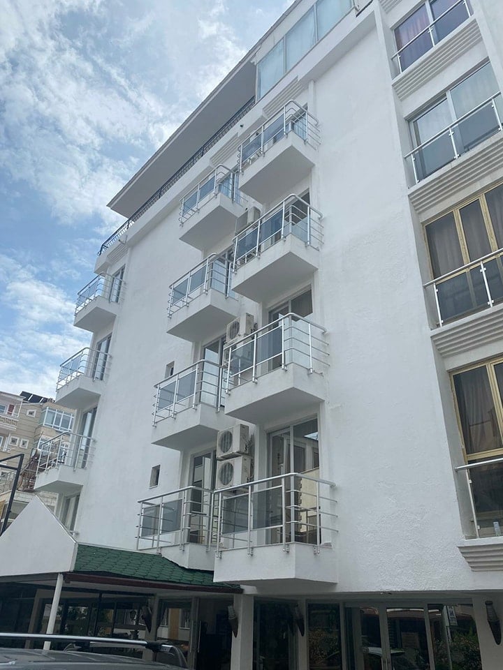 Modern white apartment building with balconies and metal railings viewed from below against a blue sky