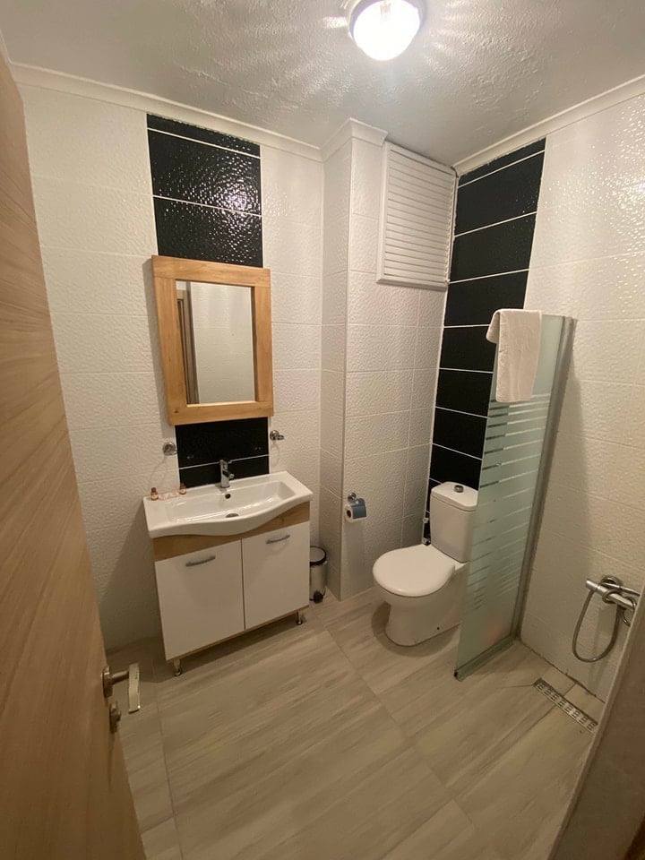 Modern bathroom interior with white vanity, wooden mirror frame, toilet, and black and white tile accents