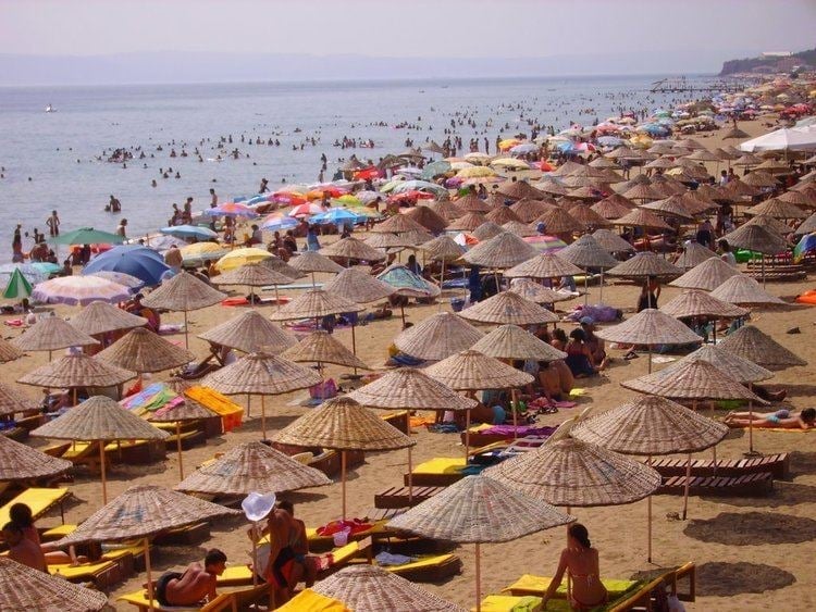 Crowded beach with dozens of straw umbrellas, colorful beach umbrellas, and swimmers in the Mediterranean Sea
