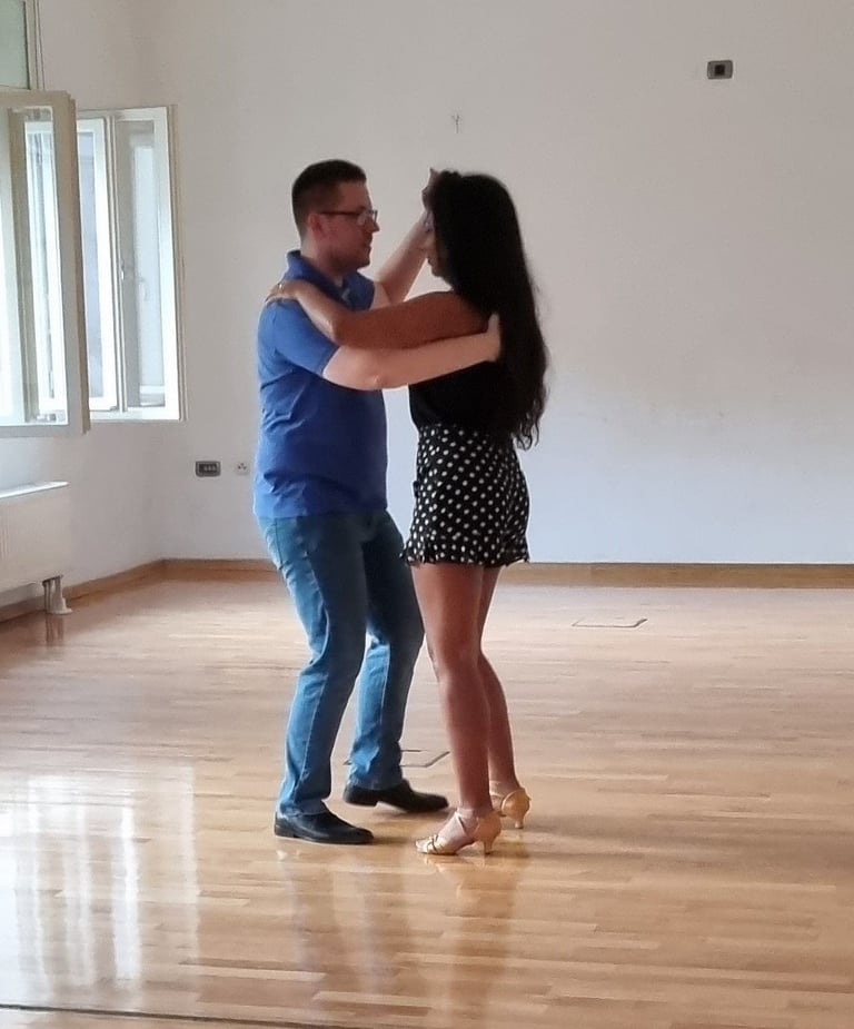 Muškarac u plavoj košulji i žena u točkastoj haljini plešu u praznoj dvorani s drvenim podom Plesne škole Banderillas