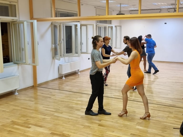 Plesni instruktor podučava polaznicu u žutoj haljini salsu u drvenoj dvorani s ogledalima Plesne škole Banderillas Zagreb