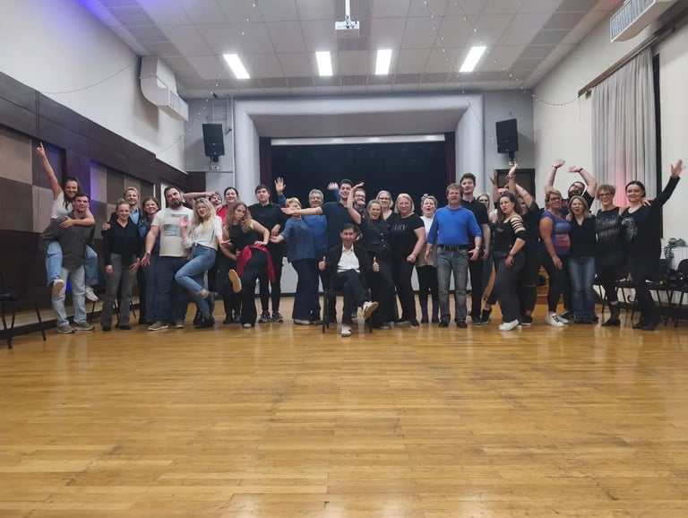 Velika grupa polaznika Plesne škole Banderillas pozira zajedno na drvenom podu dvorane pod stage rasvjetom i zvučnicima