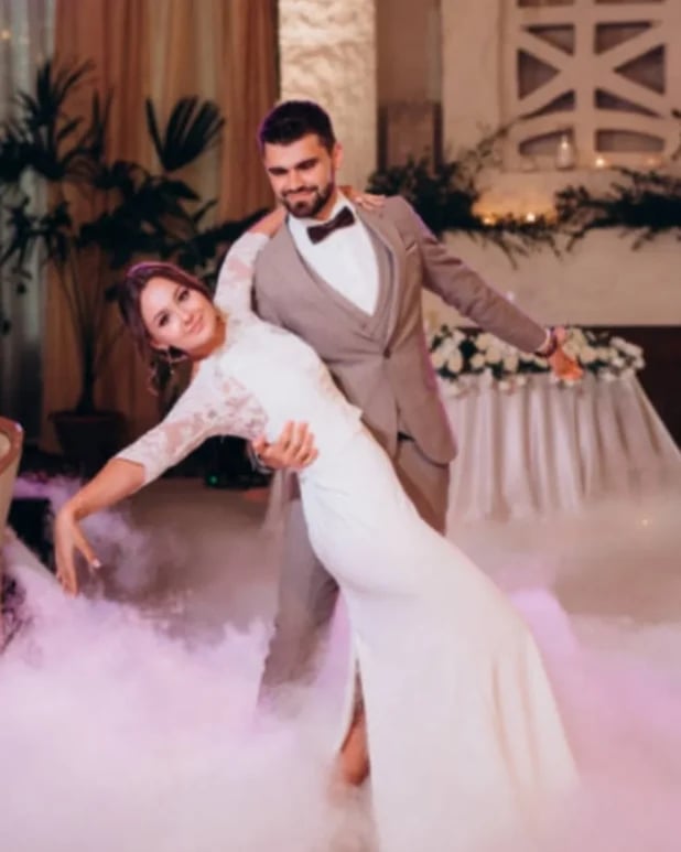 Mladenac u bež odijelu s leptir mašnom vodi mladenku u bijeloj vjenčanici u dramatičnom spustom kroz oblake dima
