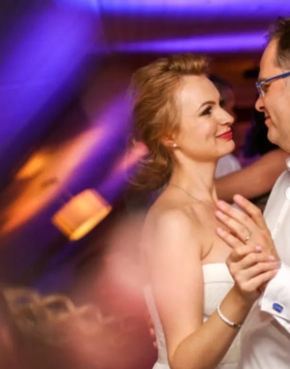 Par pleše na plesnom podiju kluba s ljubičastim i narančastim svjetlima u pozadini