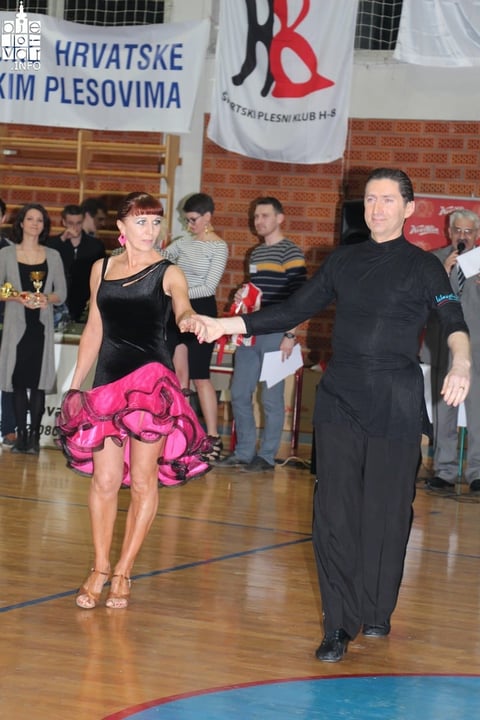 Male and female dancers performing Latin dance on wooden floor at indoor competition with audience and Croatian banners in background