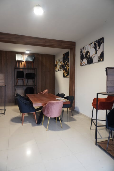 Modern dining room with round wood table, colorful upholstered chairs, dark wood frame, and abstract artwork on walls