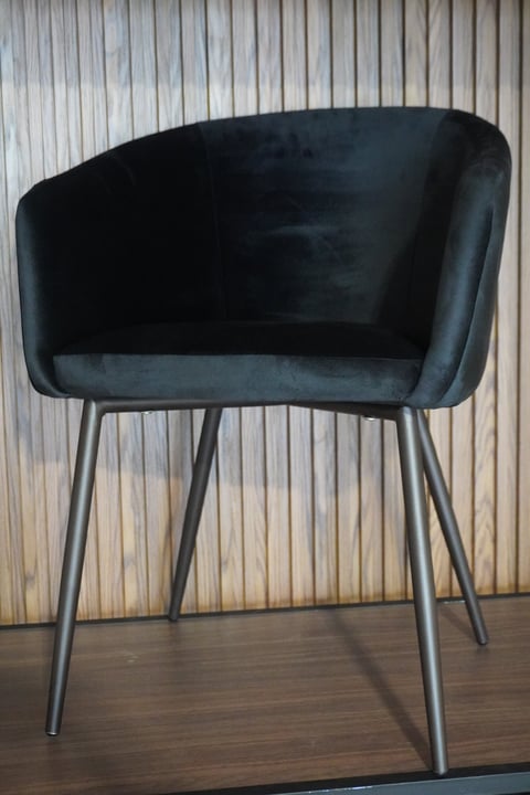 Modern black velvet accent chair with curved bucket seat and angled metal legs on wooden floor against white corrugated wall