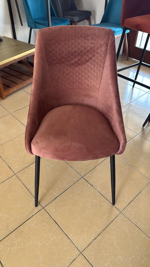 Modern dining chair with mauve upholstered seat and backrest, black metal legs, displayed in a showroom with other chairs in the background