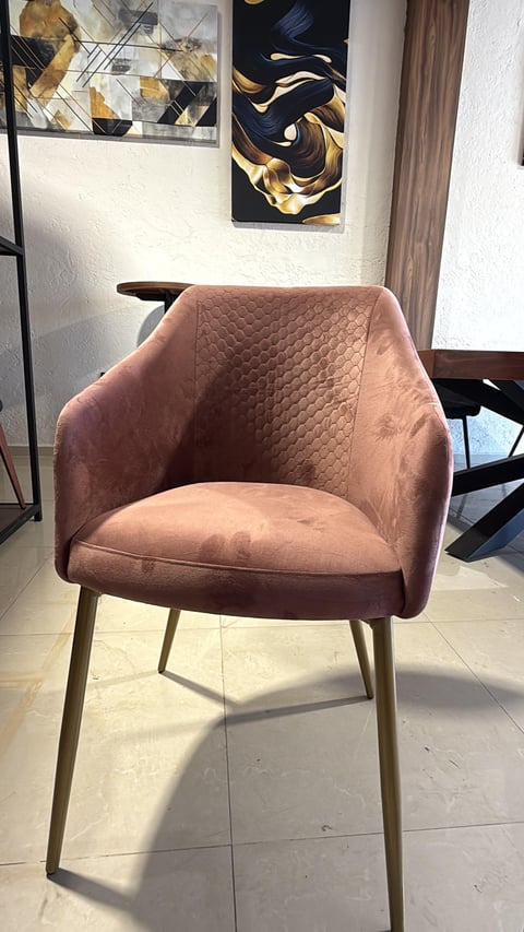 Modern blush pink velvet armchair with quilted backrest and metal legs in a minimalist interior space