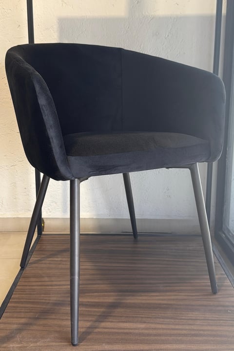 Black upholstered modern accent chair with curved back and metal legs on wooden floor near window