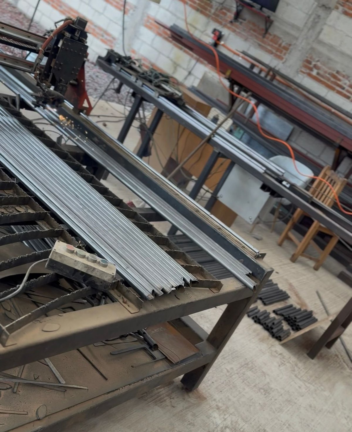 Industrial workshop with metal corrugated roofing materials stacked on tables, industrial machinery visible in background