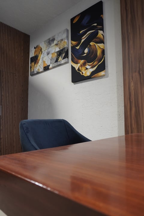 Modern office interior with wooden table, blue chair, and abstract blue and gold artwork on white walls