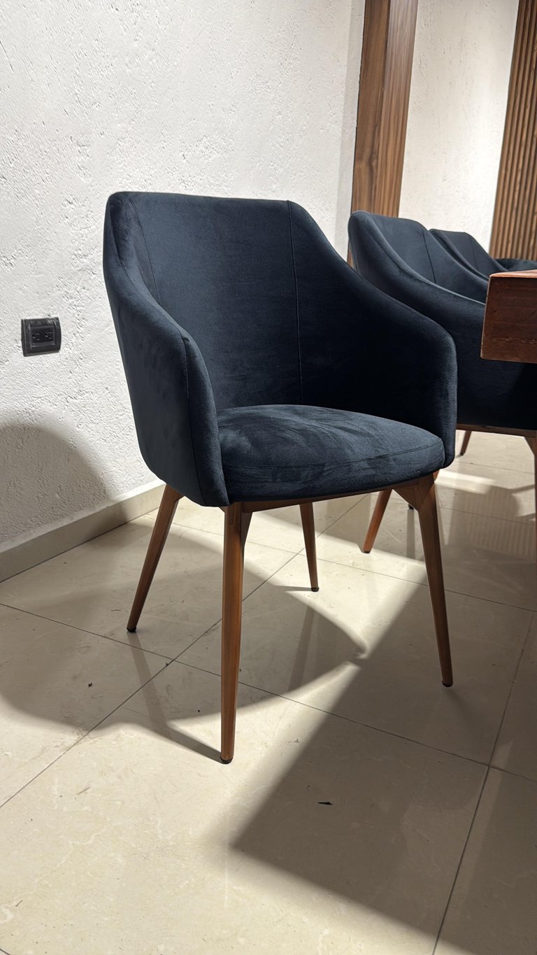 Dark blue upholstered modern armchair with wooden legs in a bright, minimalist interior space