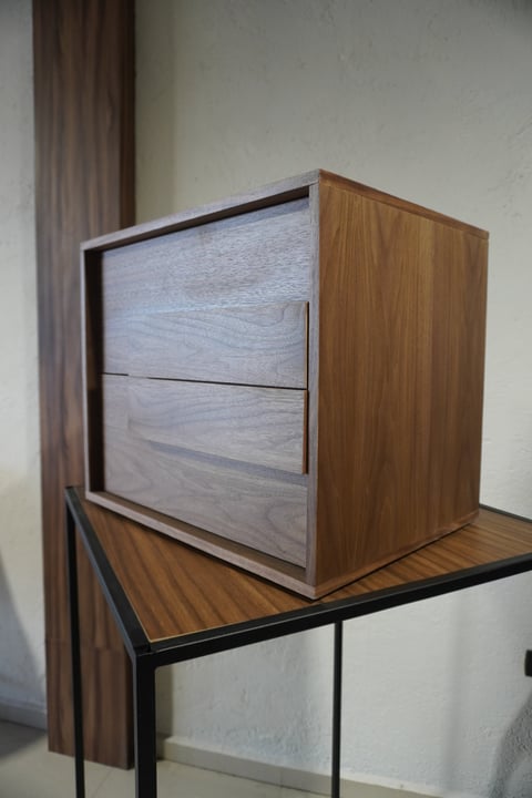 Modern wooden nightstand with two drawers sitting on a metal-legged table against a white wall